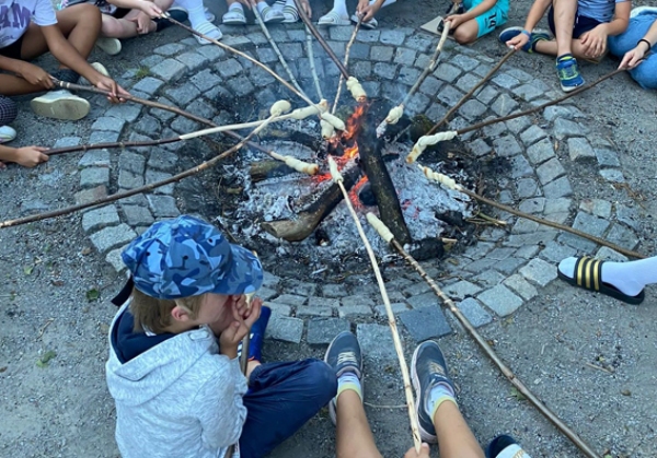 eine Gruppe von Kindern sitzt um ein Lagerfeuer, es wird Stcokbrot gegrillt