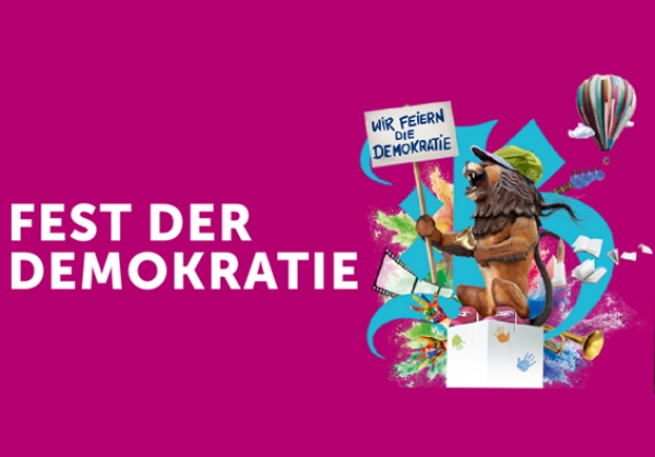 magentafarbener Hintergrund mit dem Schriftzug "Fest der Demokratie", rechts daneben das Logo mit einem stilisierten Löwen, der ein Schild hochhält auf dem "Wir feiern Demokratie" steht