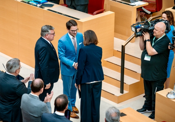 Der neue Staatsminister für Jugend und Demokratie wird im Bayerischen Landtag vereidigt und schüttelt Ilse Aigner die Hand, dvor eine reihe klatschender Politiker:innen